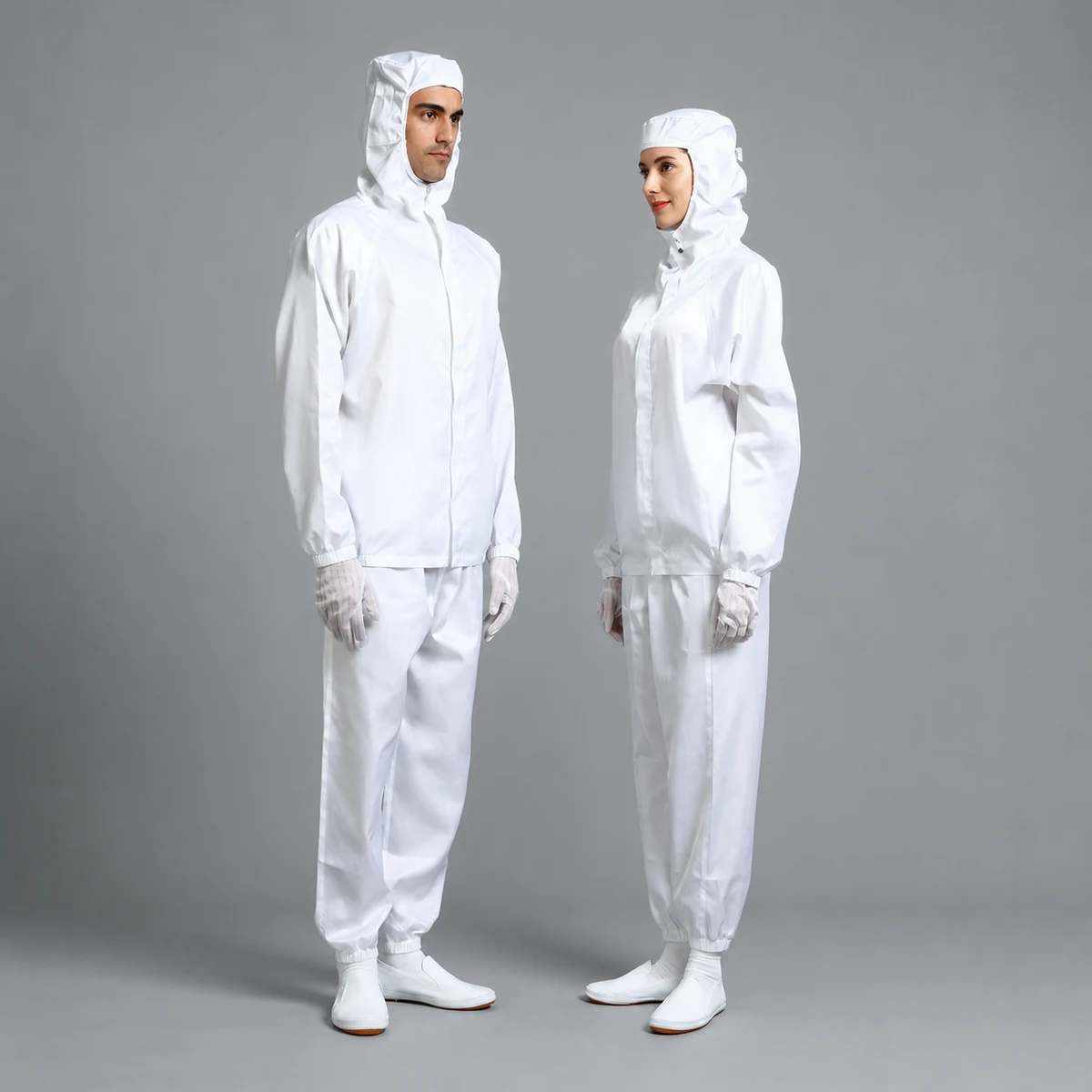 Two operators wearing white two-piece cleanroom suits with hooded jackets and separate pants