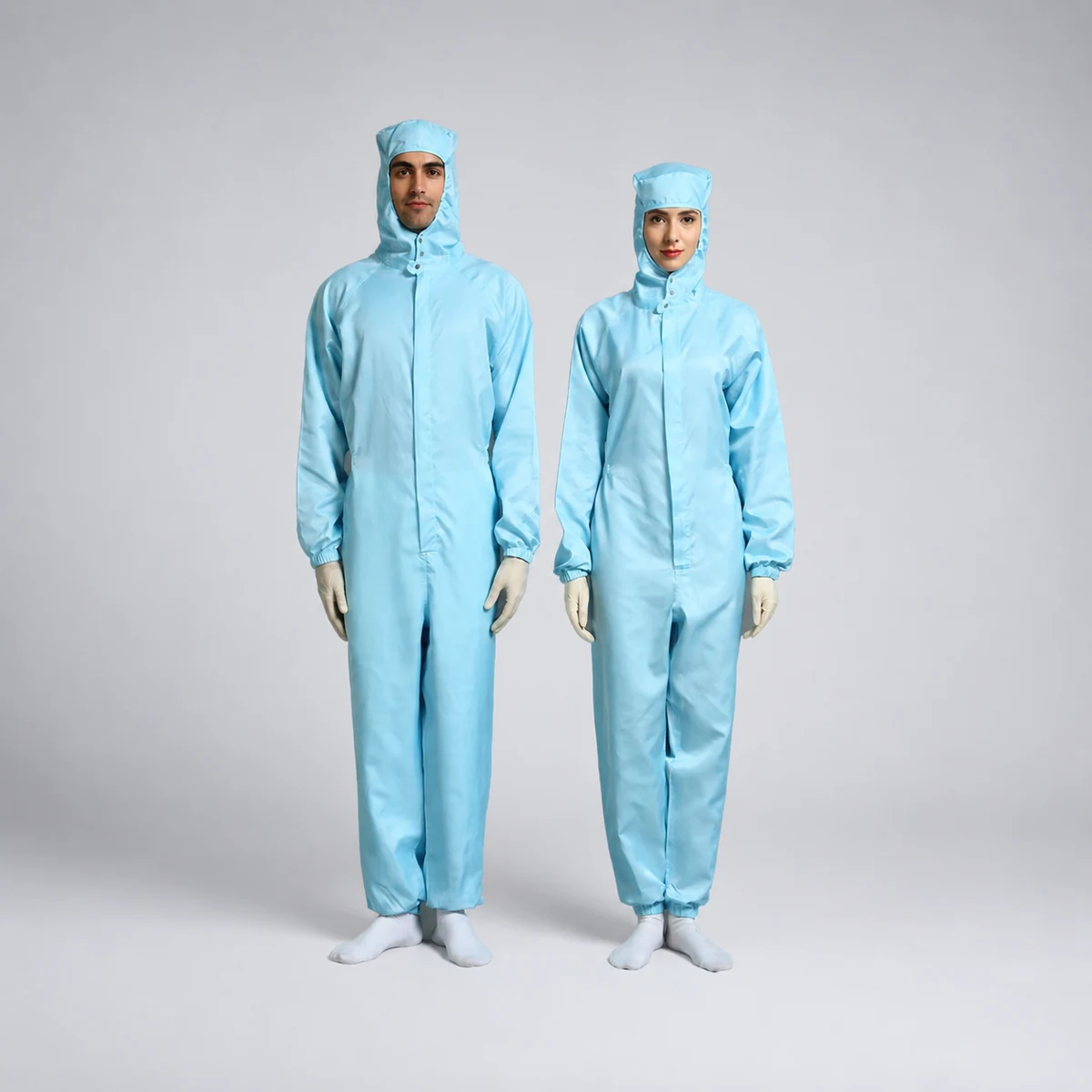 Two operators wearing light-blue one-piece hooded cleanroom coveralls